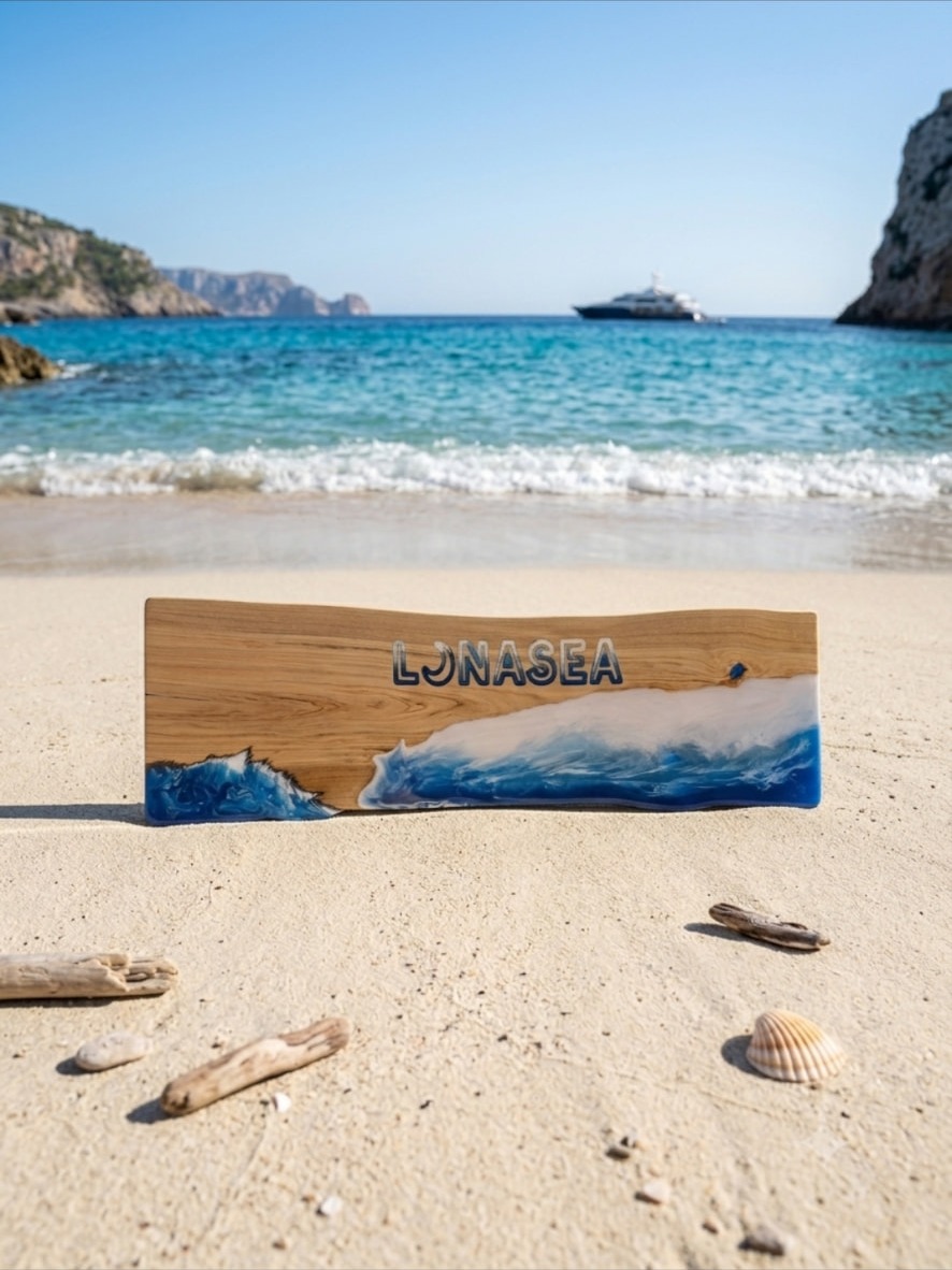 Lunasea — bespoke live-edge cherry serving board with hand-poured seafoam resin wave and carved resin-filled lettering, photographed on white sand above a turquoise Scottish-lit bay with driftwood and shells