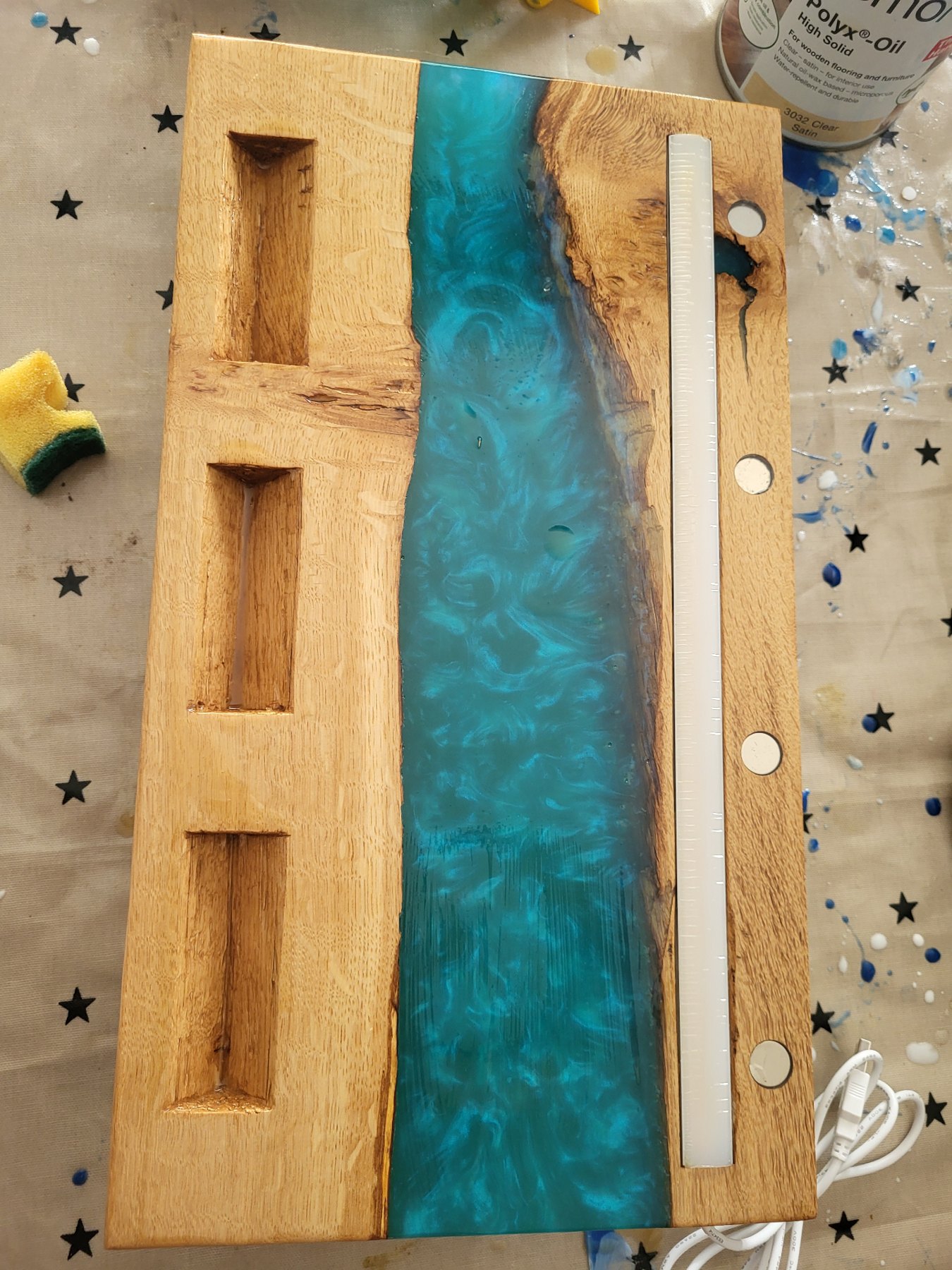 Workshop view of the Trio base — three hand-carved bottle placements in oak beside a teal resin river and the LED channel