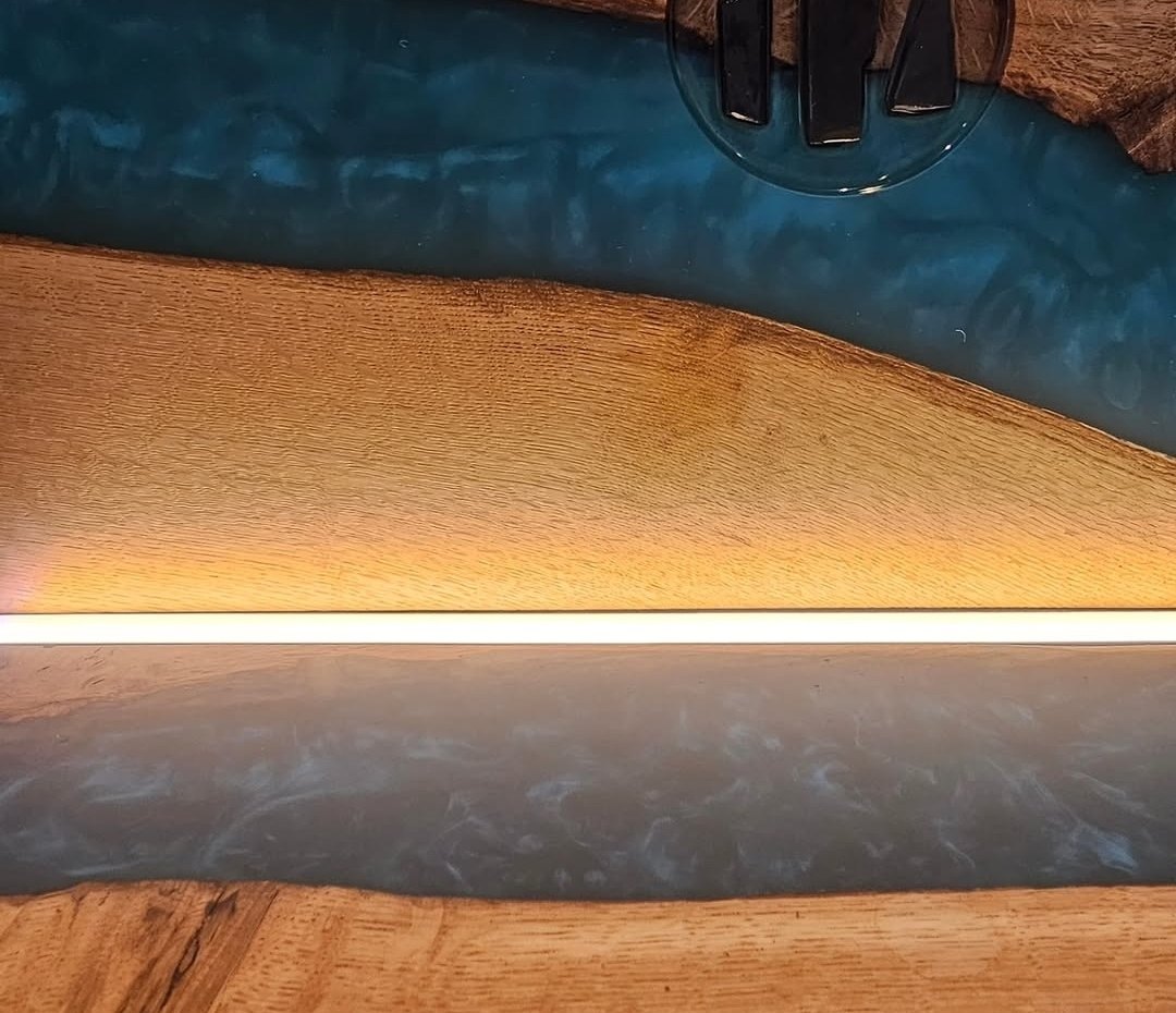 Detail of the single LED strip where backboard meets base on the Trio whisky display, light washing across teal resin and oak grain