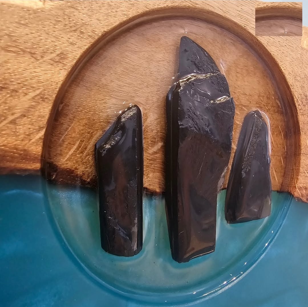 Close detail of the Tri Carragh three-pillar logo hand-cut from slate and set into clear resin over oak and teal resin